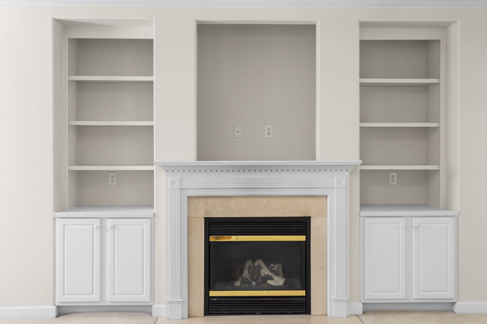 Unlit gas fireplace with a log set behind glass, set in a white mantel between built-in shelves